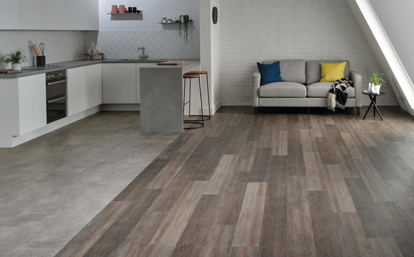 Pale concrete effect flooring in an open plan kitchen next to dark oak effect flooring in a living area
