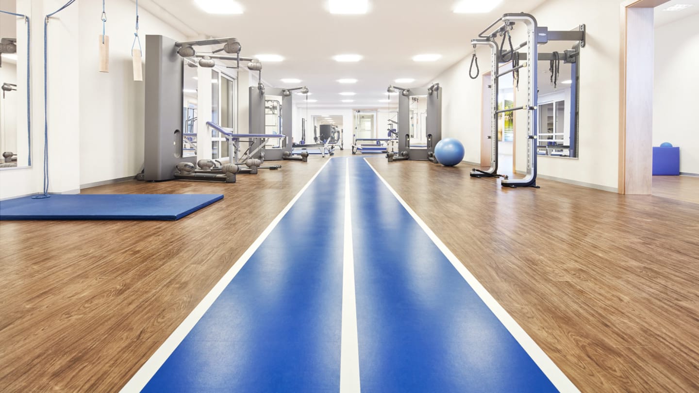 A bright blue and white path goes through the centre of a gym, with light wood-effect floor planks either side