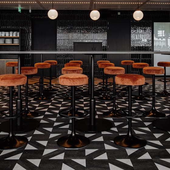 Seating area features black bar stools with orange seats, paired with black and white stone LVT flooring.