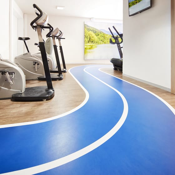 A bright blue and white path winds through a gym, with light wood-effect floor planks