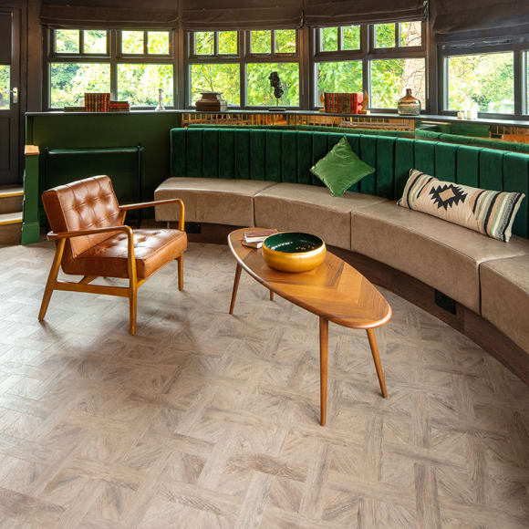Circular seating area features warm oak LVT with green velvet cushions and brown furniture.