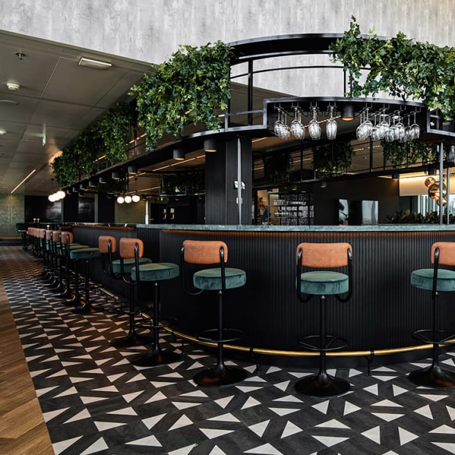 Bar features a black framed bar with orange and green bar stools, paired with black and white stone LVT flooring.