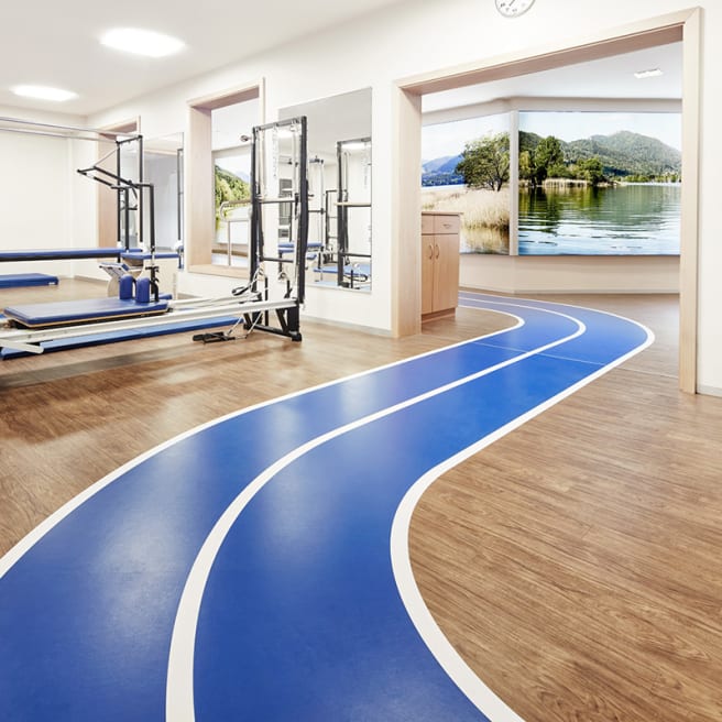 A bright blue and white path winds through a gym, with light wood-effect floor planks either side
